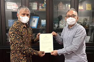 A local staff member presenting a donation certificate to a Vice President of Mulawarman University